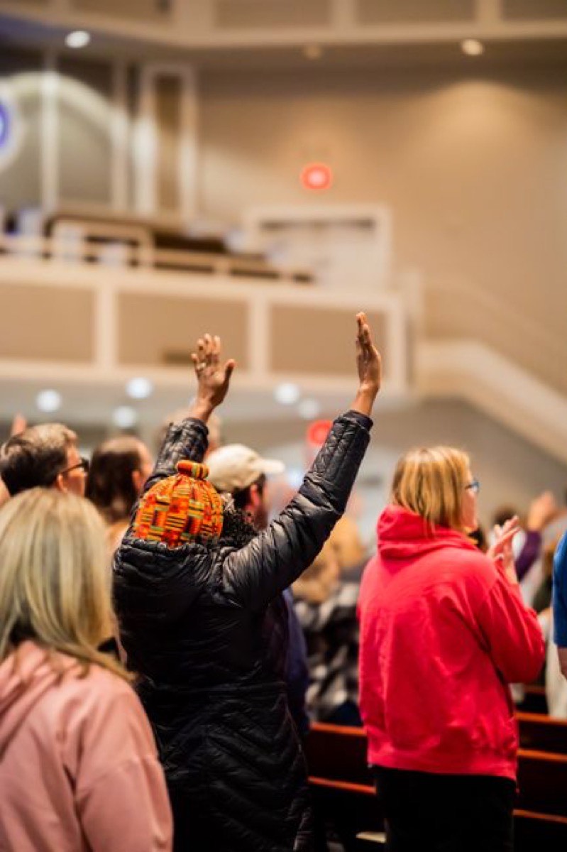 A congregation during a service, several people with hands raised.
